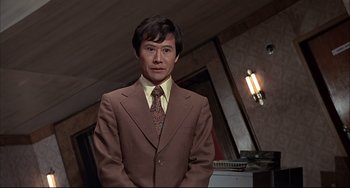 Movie still from “The Man with the Golden Gun” (1974), directed by Guy Hamilton – A man in a brown suit and a yellow tie; Medium shot, Low angle