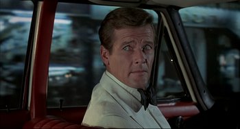 Movie still from “The Man with the Golden Gun” (1974), directed by Guy Hamilton – A person sitting in a car wearing a tie; Close Up shot, Over the shoulder angle