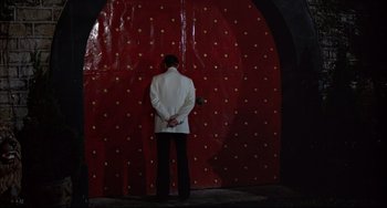 Movie still from “The Man with the Golden Gun” (1974), directed by Guy Hamilton – A man in a white jacket standing in front of a red wall; Wide shot, Over the shoulder angle