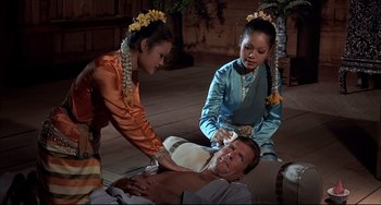 Movie still from “The Man with the Golden Gun” (1974), directed by Guy Hamilton – A couple of women standing over a man on the ground; Medium shot, High angle