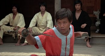 Movie still from “The Man with the Golden Gun” (1974), directed by Guy Hamilton – A young man holding a sword in front of two other men; Medium shot, Low angle