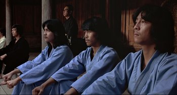 Movie still from “The Man with the Golden Gun” (1974), directed by Guy Hamilton – A group of young men sitting next to each other; Medium shot, Low angle