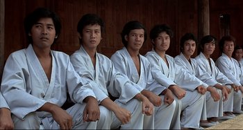 Movie still from “The Man with the Golden Gun” (1974), directed by Guy Hamilton – A group of young men sitting in front of each other; Medium shot, High angle