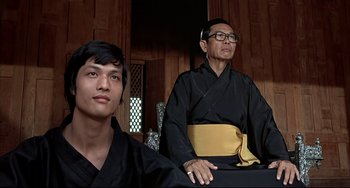 Movie still from “The Man with the Golden Gun” (1974), directed by Guy Hamilton – A man and a young man in black robes; Medium shot, Low angle