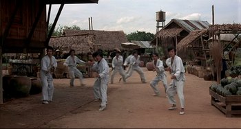 Movie still from “The Man with the Golden Gun” (1974), directed by Guy Hamilton – A group of men in white uniforms practicing martial arts in an open area; Wide shot, High angle