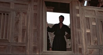 Movie still from “The Man with the Golden Gun” (1974), directed by Guy Hamilton – A woman standing in the window of an old house; Wide shot, Low angle