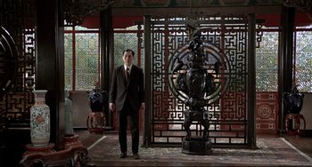 Movie still from “The Man with the Golden Gun” (1974), directed by Guy Hamilton – A man in a suit standing next to a statue; Wide shot, Low angle