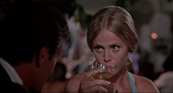Movie still from “The Man with the Golden Gun” (1974), directed by Guy Hamilton – A woman drinking a glass of white wine while a man looks on; Close Up shot, Over the shoulder angle