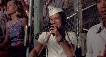 Movie still from “The Man with the Golden Gun” (1974), directed by Guy Hamilton – A man wearing a white hat is holding a cell phone; Close Up shot, Low angle
