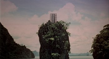 Movie still from “The Man with the Golden Gun” (1974), directed by Guy Hamilton – A large rock with trees on top of it near the ocean; Extreme Wide shot, Low angle