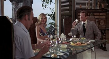 Movie still from “The Man with the Golden Gun” (1974), directed by Guy Hamilton – A group of people sitting around a table with wine glasses; Medium shot, Over the shoulder angle