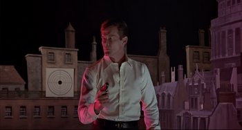 Movie still from “The Man with the Golden Gun” (1974), directed by Guy Hamilton – A man in a white shirt holding a cell phone; Medium shot, Low angle