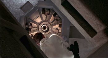 Movie still from “The Man with the Golden Gun” (1974), directed by Guy Hamilton – A woman in a white shirt is looking up at a machine; Wide shot, Overhead angle