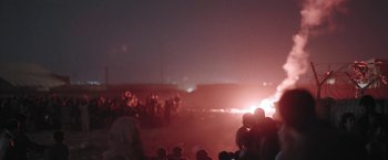 Movie still from “Retrograde” (2022), directed by Matthew Heineman – A group of people standing in a field at night; Extreme Wide shot, Low angle
