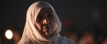 Movie still from “Retrograde” (2022), directed by Matthew Heineman – An older woman wearing a head scarf and a white shirt; Close Up shot, Low angle