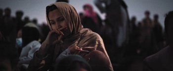 Movie still from “Retrograde” (2022), directed by Matthew Heineman – A woman holding a baby in her arms and wearing a headscarf; Close Up shot, Low angle