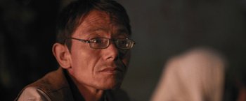 Movie still from “Retrograde” (2022), directed by Matthew Heineman – An older man with glasses looking at the camera; Close Up shot, High angle