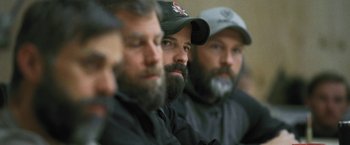 Movie still from “Retrograde” (2022), directed by Matthew Heineman – A group of men sitting next to each other wearing hats; Close Up shot, Over the shoulder angle