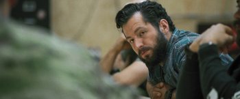 Movie still from “Retrograde” (2022), directed by Matthew Heineman – A man with a goatee and a beard is leaning on a wall; Close Up shot, Over the shoulder angle