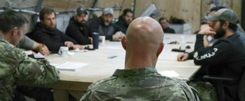 Movie still from “Retrograde” (2022), directed by Matthew Heineman – A group of men sitting around a table; Medium shot, Over the shoulder angle