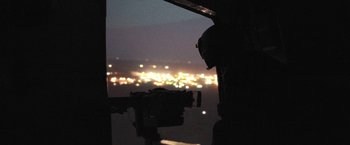 Movie still from “Retrograde” (2022), directed by Matthew Heineman – A man standing inside of an airplane looking out the window; Extreme Wide shot, High angle