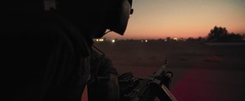 Movie still from “Retrograde” (2022), directed by Matthew Heineman – A soldier with a rifle in a field at night; Medium shot, Over the shoulder angle