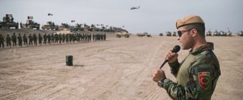 Movie still from “Retrograde” (2022), directed by Matthew Heineman – A group of people standing in the dirt; Medium shot, Over the shoulder angle