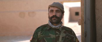 Movie still from “Retrograde” (2022), directed by Matthew Heineman – A man with a beard wearing a camouflage jacket; Close Up shot, Low angle