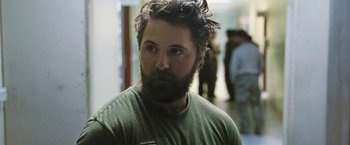 Movie still from “Retrograde” (2022), directed by Matthew Heineman – A man with a beard is standing in a room; Close Up shot, Over the shoulder angle