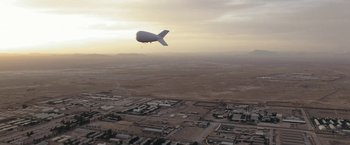 Movie still from “Retrograde” (2022), directed by Matthew Heineman – An airship flying over a city in the middle of the desert; Extreme Wide shot, Low angle