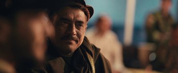 Movie still from “Retrograde” (2022), directed by Matthew Heineman – An older man wearing a brown hat and a brown scarf; Close Up shot, Over the shoulder angle