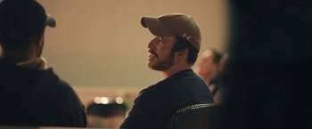 Movie still from “Retrograde” (2022), directed by Matthew Heineman – A man wearing a baseball cap sitting in front of a microphone; Close Up shot, Over the shoulder angle