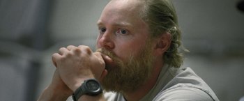 Movie still from “Retrograde” (2022), directed by Matthew Heineman – A person with a beard wearing a watch; Close Up shot, Over the shoulder angle