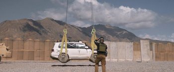 Movie still from “Retrograde” (2022), directed by Matthew Heineman – A man standing in front of a white car; Wide shot, Low angle