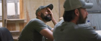 Movie still from “Retrograde” (2022), directed by Matthew Heineman – A man with a beard and a hat is sitting in front of another man; Close Up shot, Over the shoulder angle