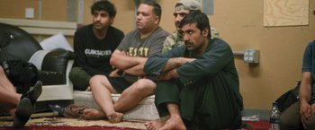 Movie still from “Retrograde” (2022), directed by Matthew Heineman – A group of men sitting next to each other on the ground; Medium shot, High angle