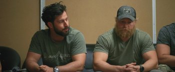 Movie still from “Retrograde” (2022), directed by Matthew Heineman – Two men sitting next to each other on a couch; Medium shot, Over the shoulder angle