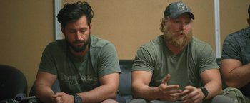 Movie still from “Retrograde” (2022), directed by Matthew Heineman – Two men sitting next to each other on a couch; Close Up shot, Over the shoulder angle