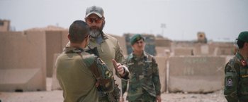 Movie still from “Retrograde” (2022), directed by Matthew Heineman – A man in a military uniform talking to two other men in fatigues; Medium shot, Over the shoulder angle