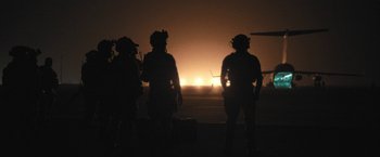 Movie still from “Retrograde” (2022), directed by Matthew Heineman – A group of soldiers standing in front of an airport runway; Wide shot, Low angle