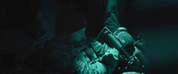 Movie still from “Retrograde” (2022), directed by Matthew Heineman – A man in camouflage sitting in a dark room; Medium shot, Over the shoulder angle