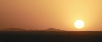Movie still from “Retrograde” (2022), directed by Matthew Heineman – The sun is setting over a large desert plain; Extreme Wide shot, Low angle