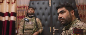 Movie still from “Retrograde” (2022), directed by Matthew Heineman – Two men in military fatigues are standing next to each other in front of a wall; Close Up shot, Over the shoulder angle