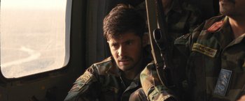 Movie still from “Retrograde” (2022), directed by Matthew Heineman – A man with a gun in his hand and wearing a camouflage uniform; Close Up shot, Low angle