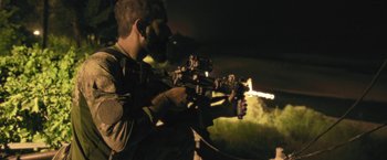 Movie still from “Retrograde” (2022), directed by Matthew Heineman – A man holding a gun while standing in the dark; Medium shot, Low angle