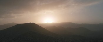 Movie still from “Retrograde” (2022), directed by Matthew Heineman – The sun is setting over a mountain range; Extreme Wide shot, Low angle