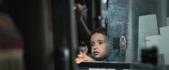 Movie still from “Retrograde” (2022), directed by Matthew Heineman – A young boy looking out a window on a train; Extreme Close Up shot, Low angle
