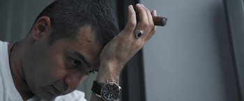 Movie still from “Retrograde” (2022), directed by Matthew Heineman – A person wearing a watch and holding a cigar; Close Up shot, Low angle