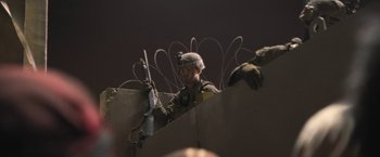 Movie still from “Retrograde” (2022), directed by Matthew Heineman – A man in a helmet is holding a rifle; Medium shot, Low angle