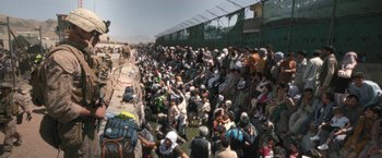 Movie still from “Retrograde” (2022), directed by Matthew Heineman – A large group of people are gathered around a fence; Extreme Wide shot, High angle